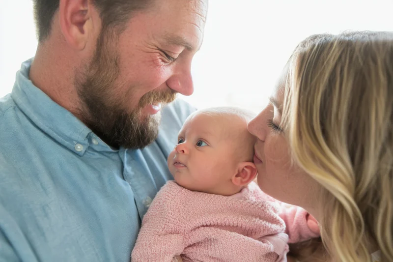 Parents smiling and kissing their newborn baby held close indoors