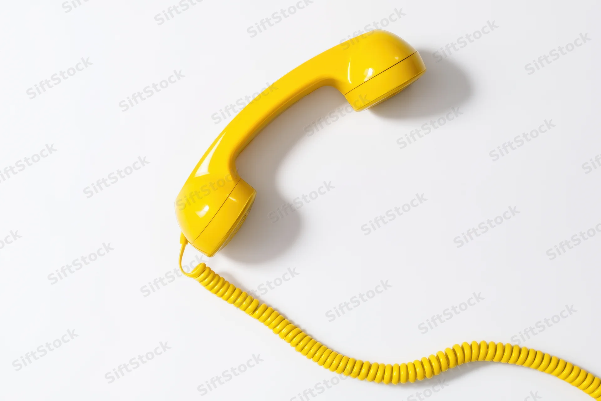 Bright yellow corded telephone handset lying on a white surface with coiled cord extending to the side