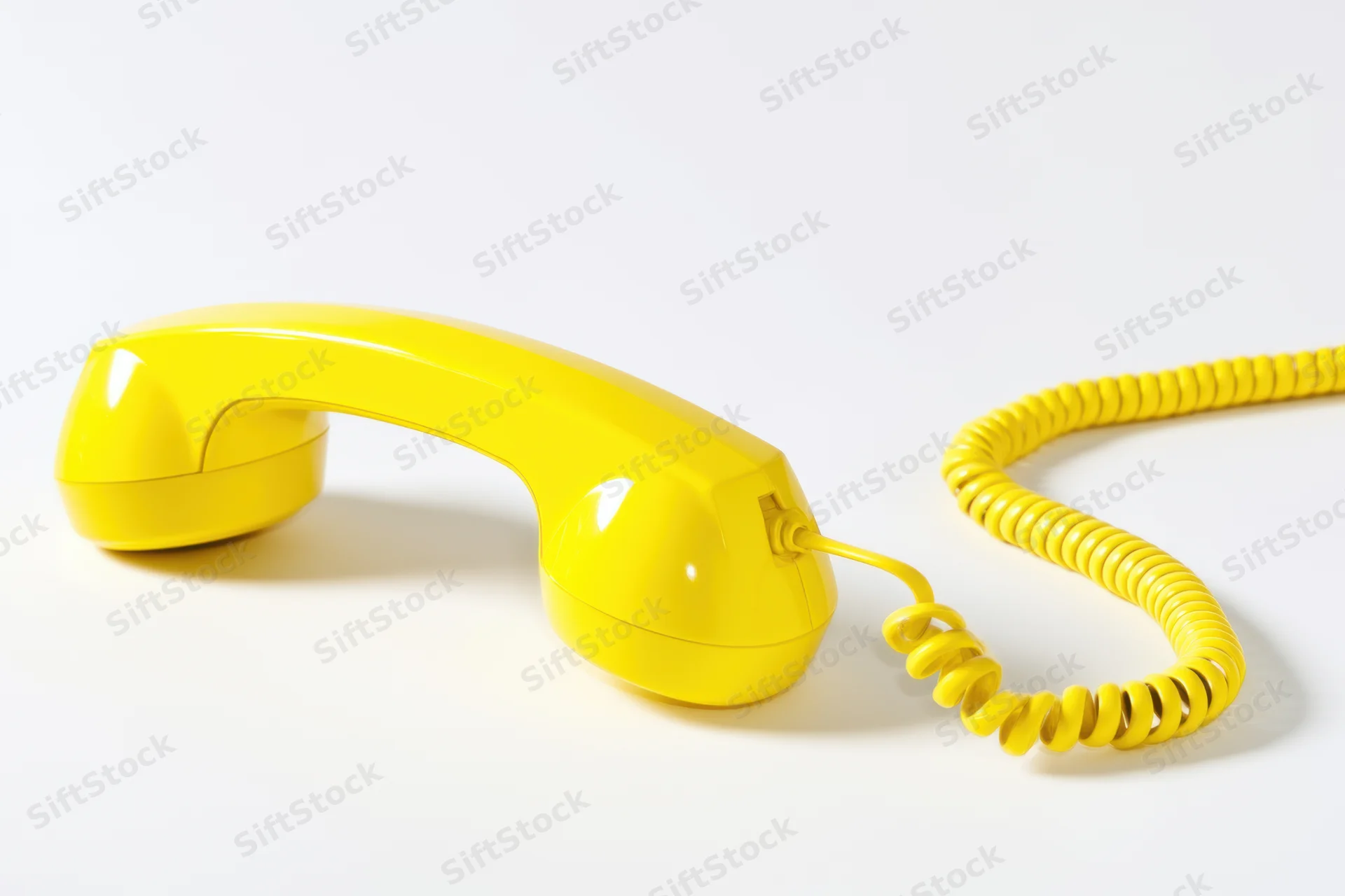 Bright yellow corded telephone handset lying on a white background with coiled cord extending to the side