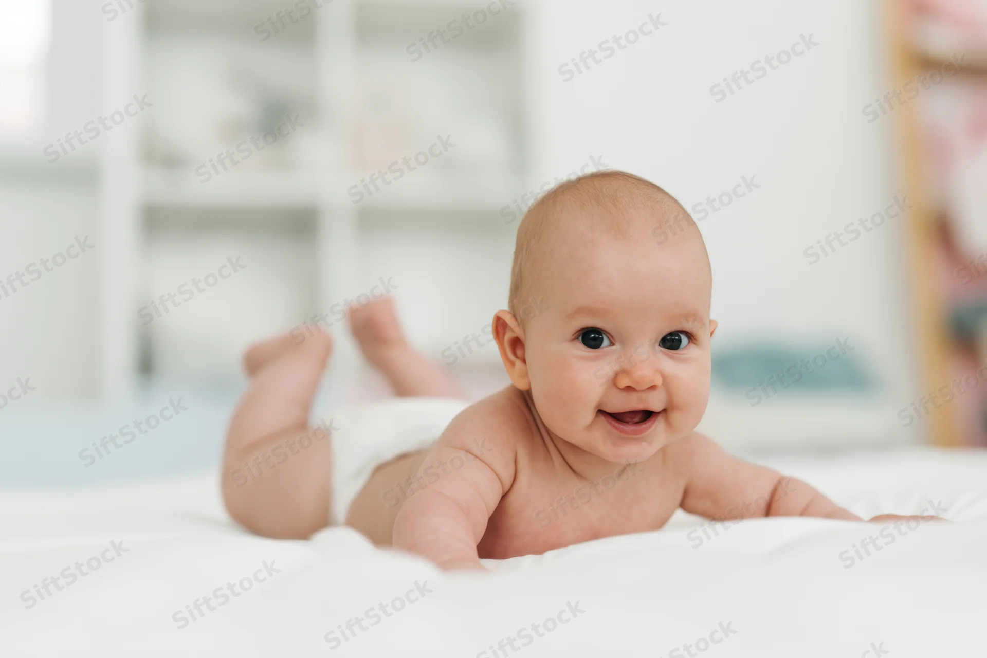 Baby lying on stomach on white surface smiling with diaper on