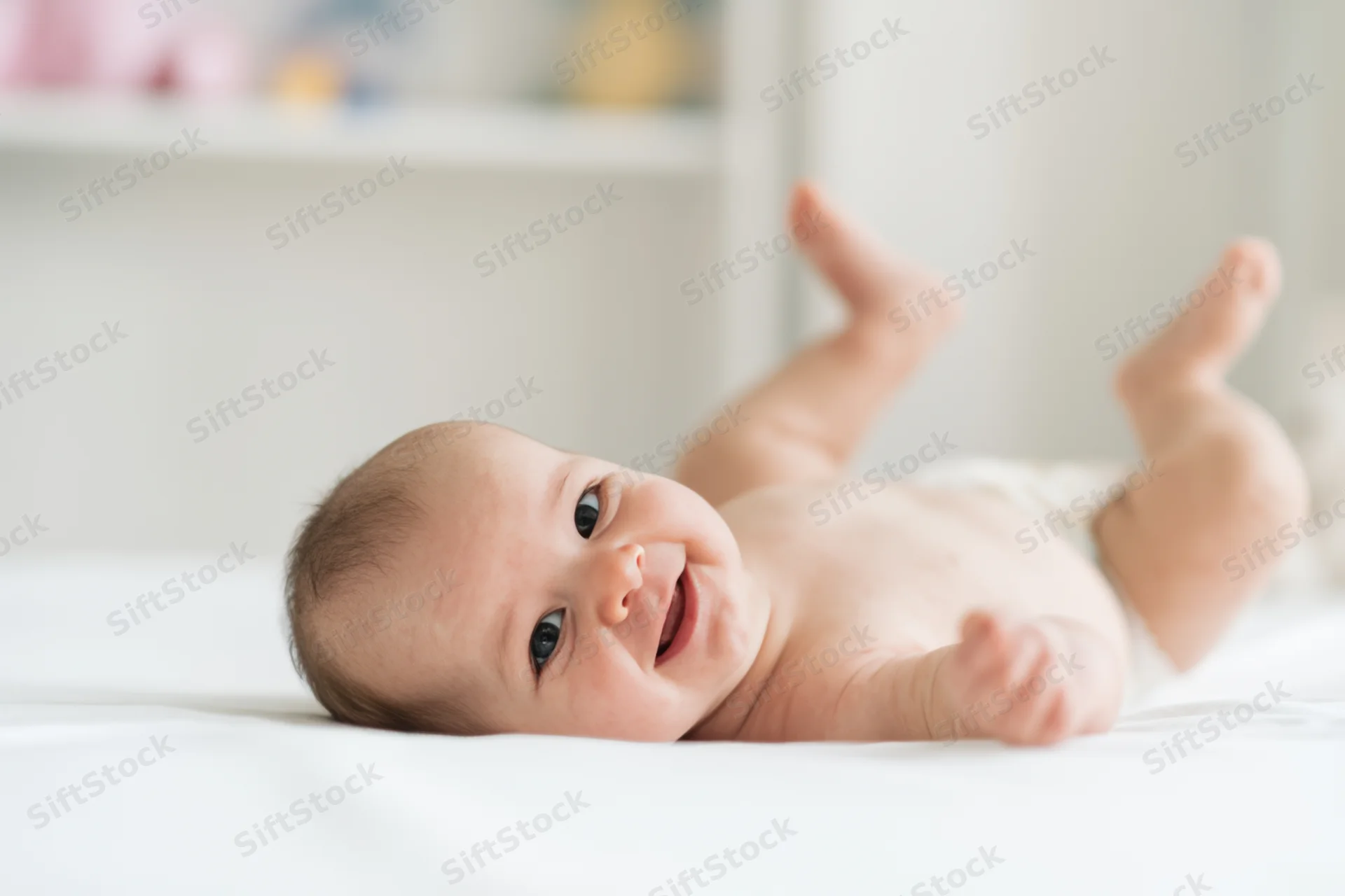Smiling baby lying on white surface wearing diaper