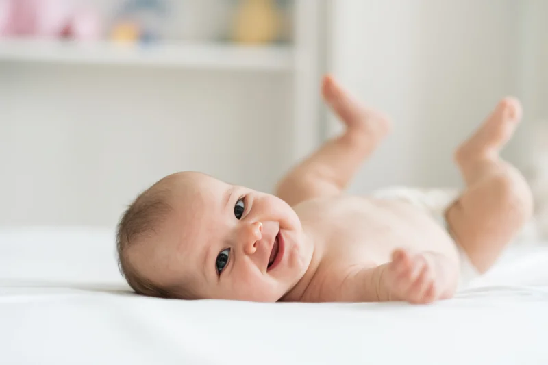 Smiling baby lying on white surface wearing diaper