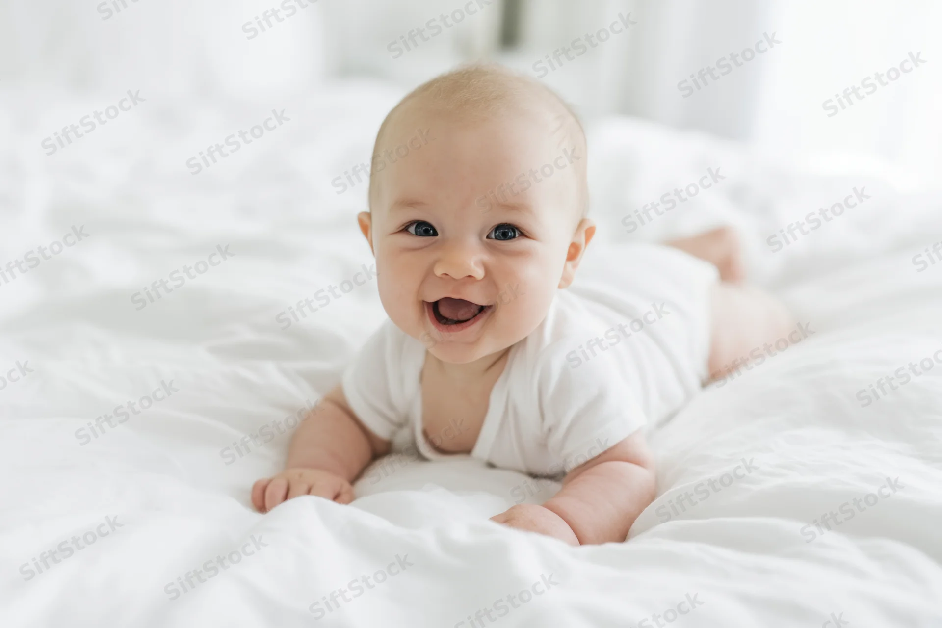 Baby lying on stomach on white bed smiling widely