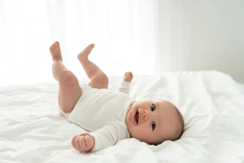 Smiling baby lying on white bed wearing white onesie