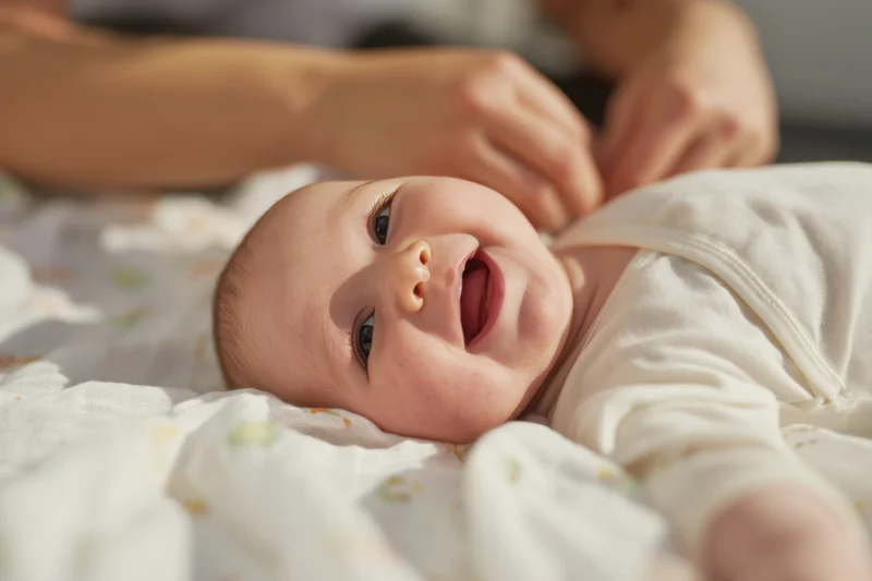 Baby lying on patterned blanket smiling with open mouth and bright eyes