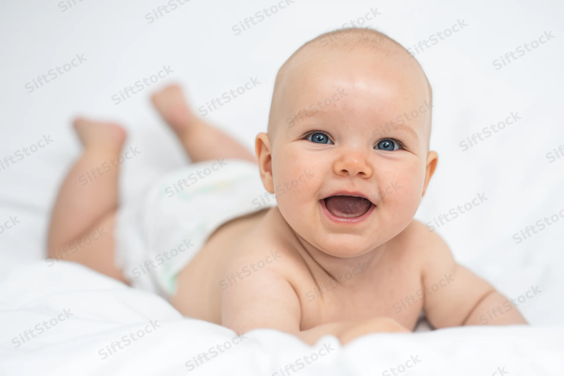 Baby lying on white surface smiling with diaper on