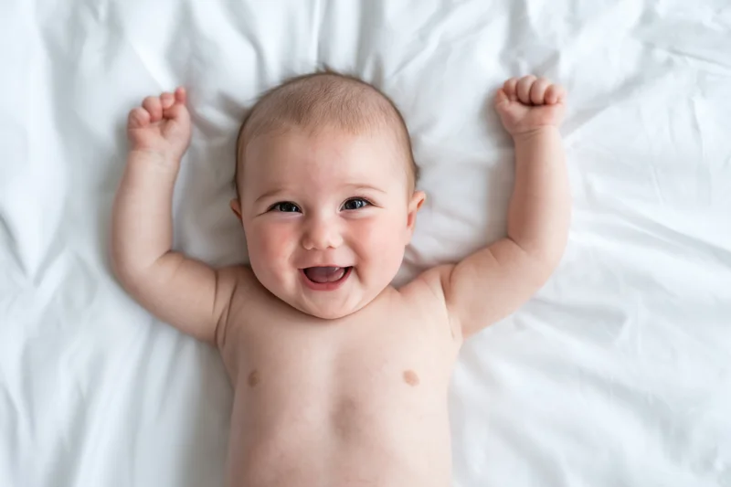 Baby lying on white soft surface with arms raised smiling