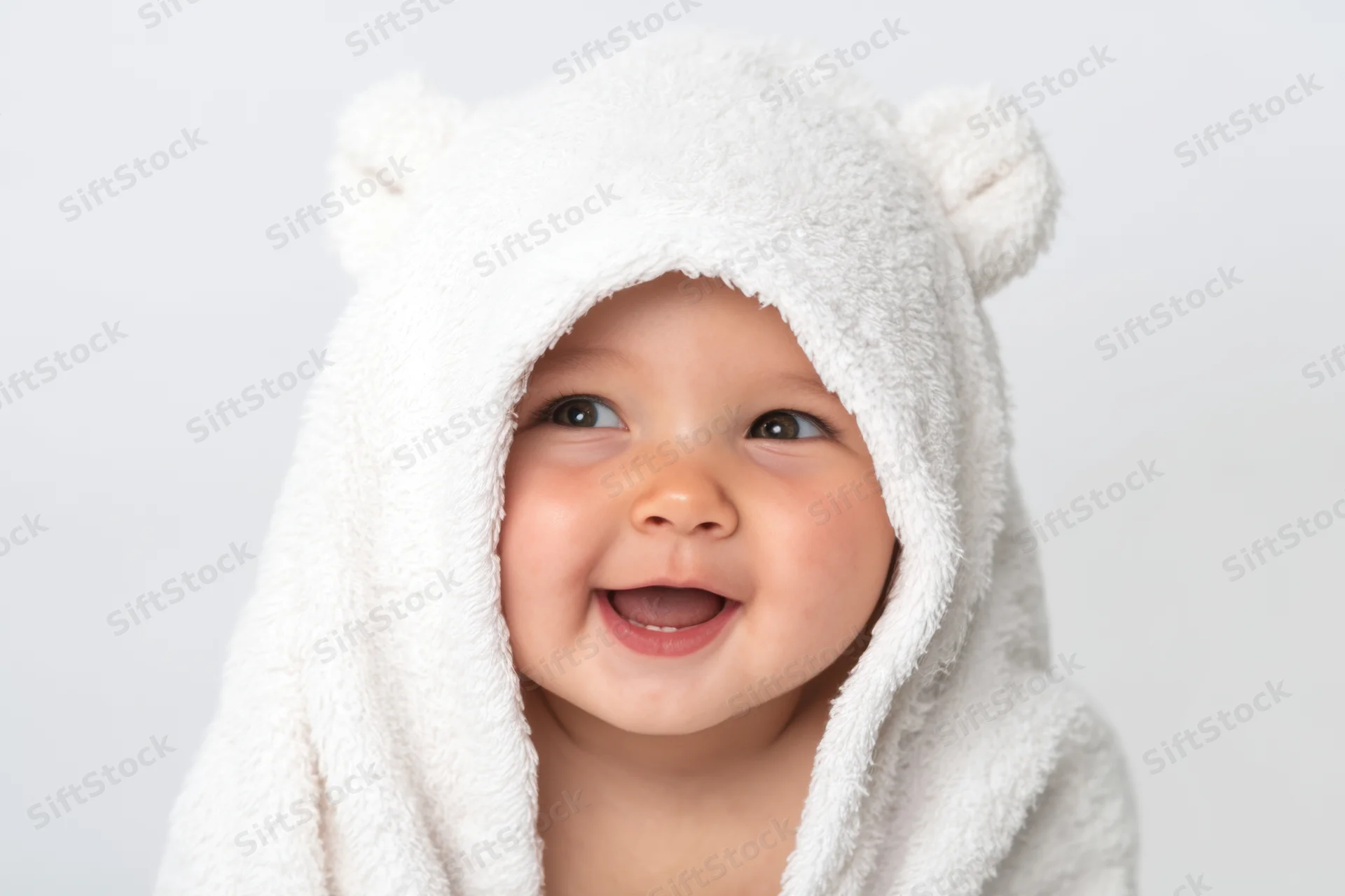 Baby wrapped in a fluffy white hooded towel with bear ears smiling happily