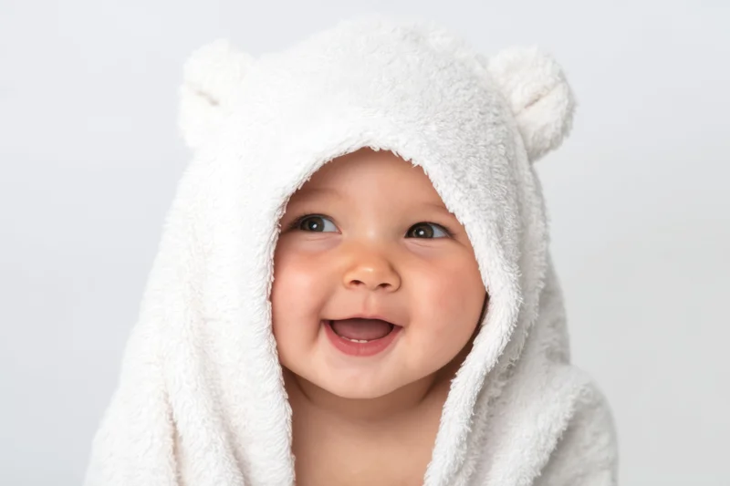 Baby wrapped in a fluffy white hooded towel with bear ears smiling happily