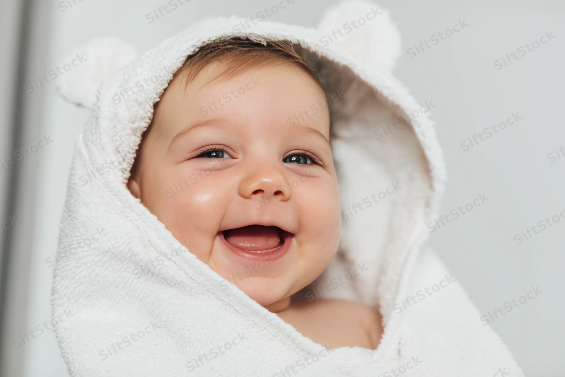 Baby wrapped in a fluffy white hooded towel smiling broadly indoors