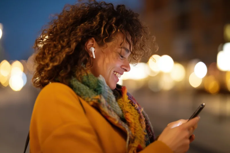 Woman smiling while using smartphone outdoors at night in city setting