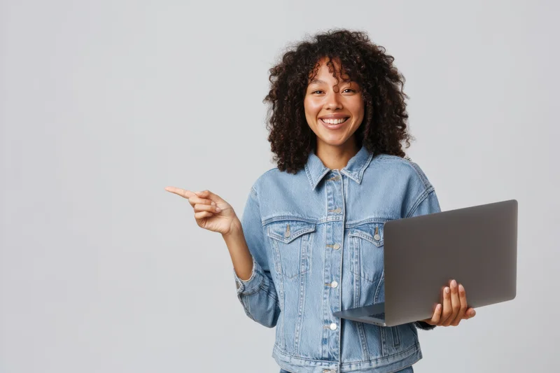 Smiling woman pointing while holding laptop in studio setting