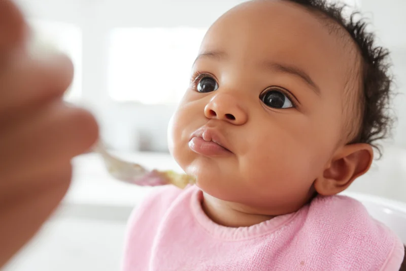 Baby in pink bib looking up at spoon during feeding time