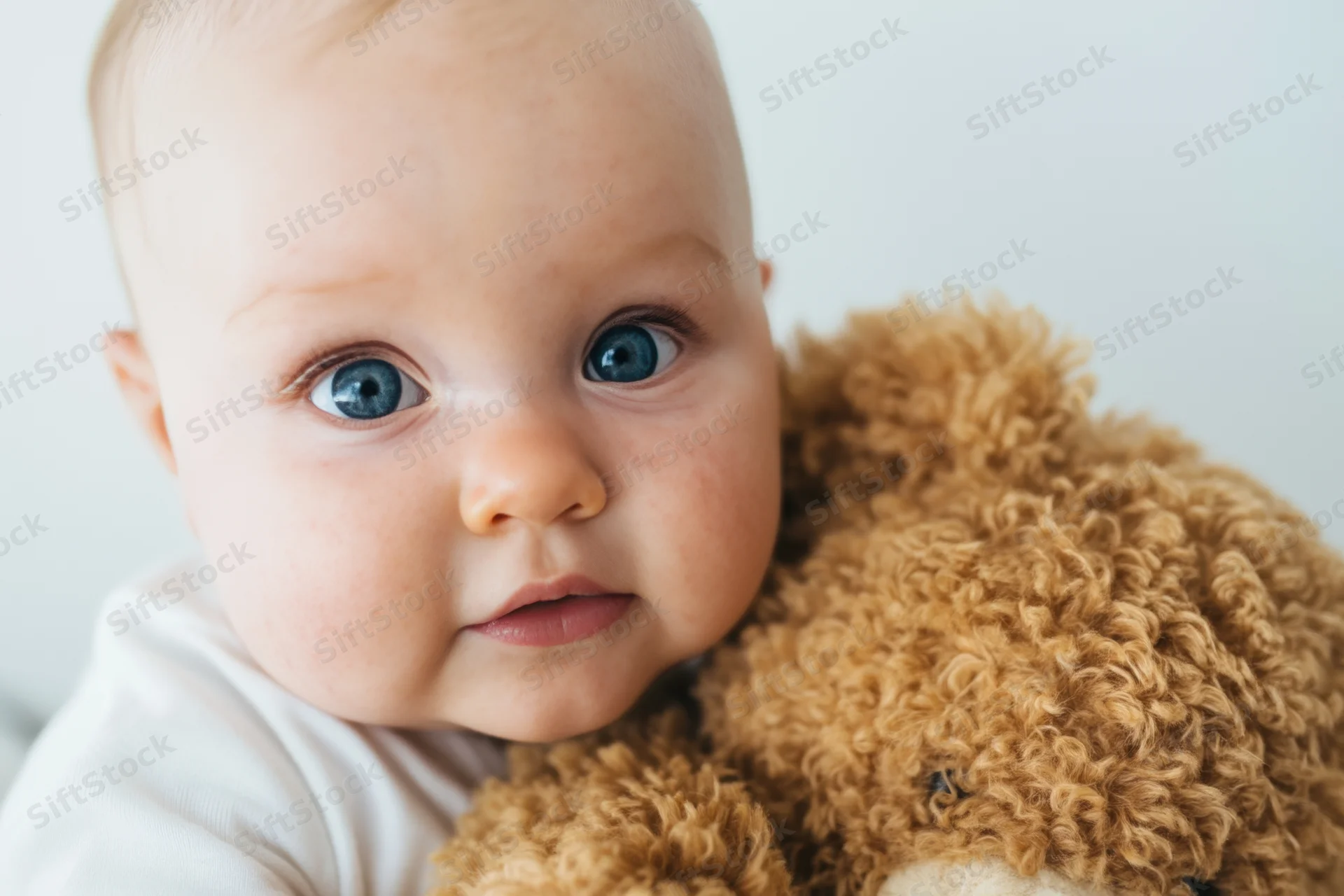 Baby hugging a fluffy brown teddy bear indoors with soft natural light