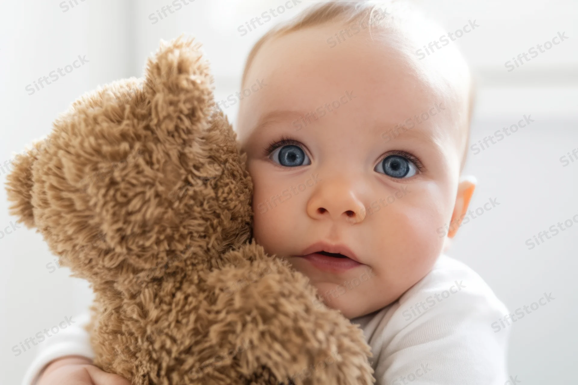 Baby hugging a fluffy brown teddy bear indoors with soft lighting and copyspace in the background