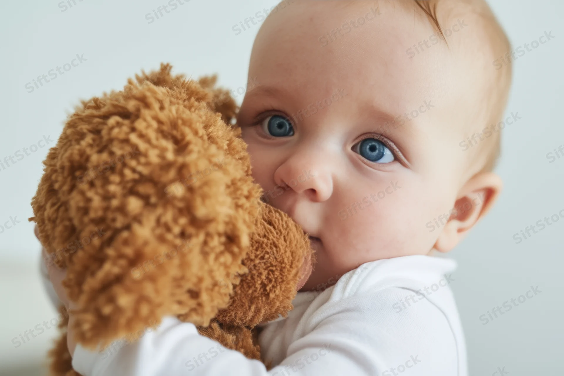 Baby hugging a fluffy brown teddy bear in a close-up portrait