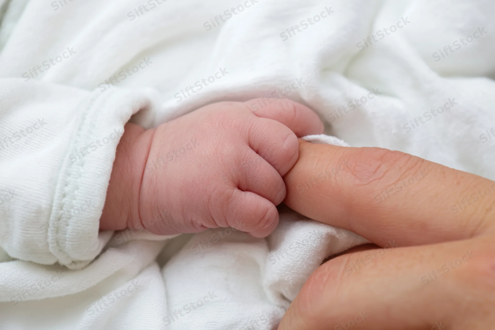 Newborn baby’s hand gripping an adult finger on a white blanket