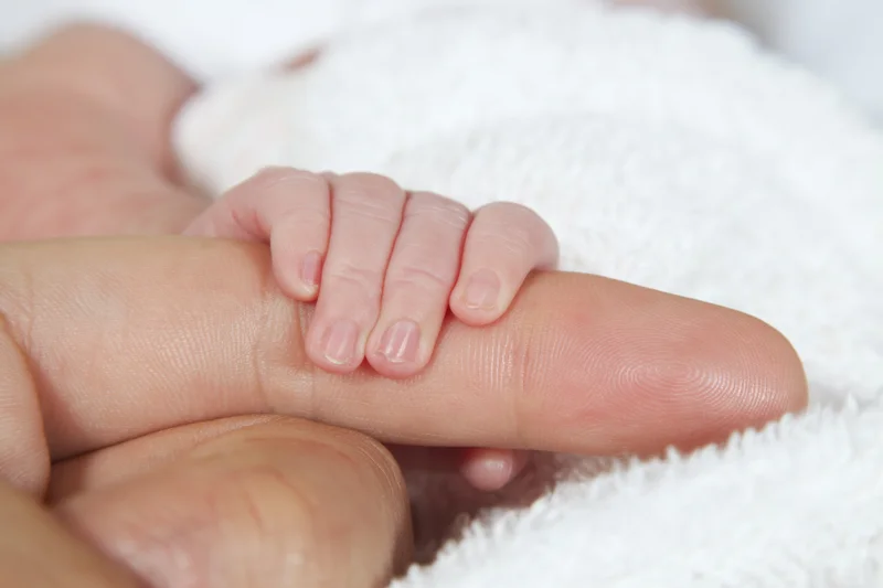 Baby's small hand gripping an adult finger on a white towel