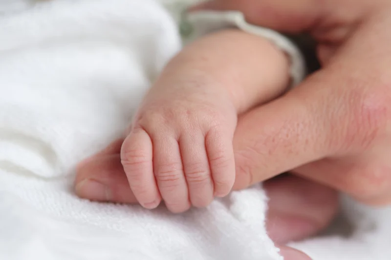 Baby's small hand gripping an adult finger on a white towel