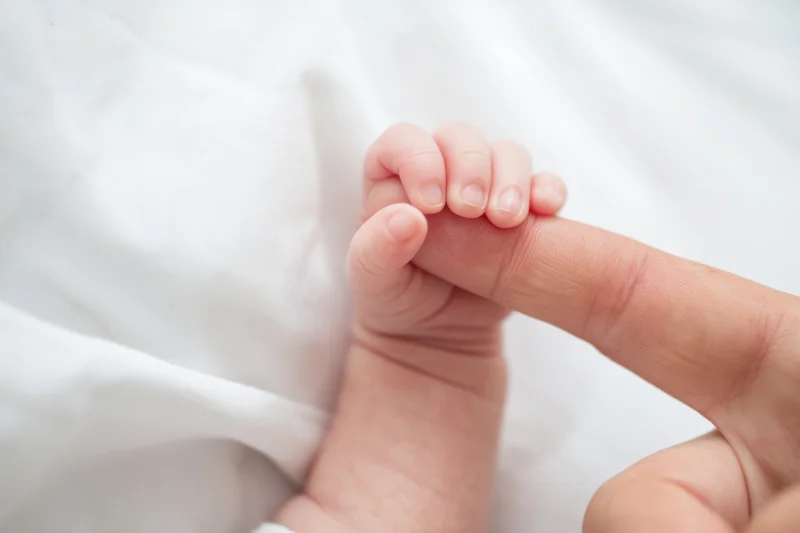 Newborn baby's hand gripping an adult finger on a white blanket