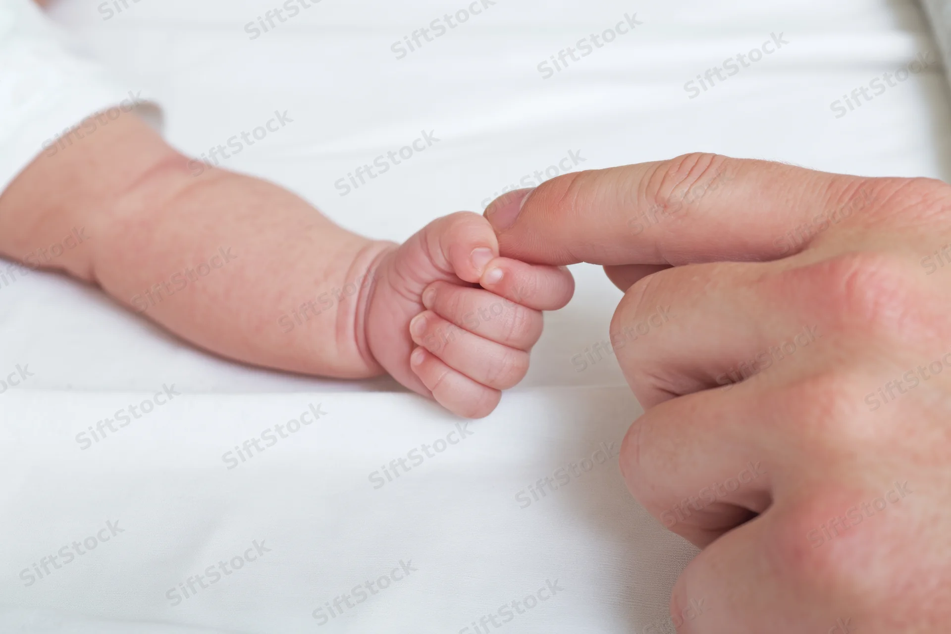 Newborn baby's hand holding adult finger on white blanket