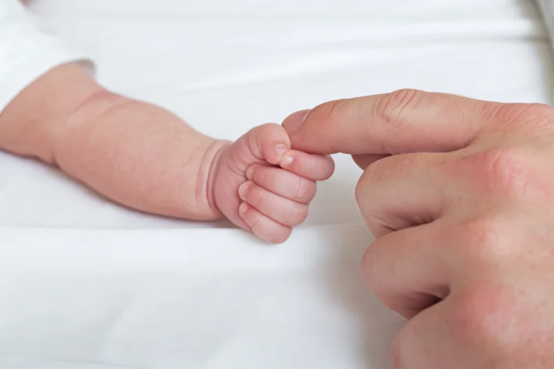 Newborn baby's hand holding adult finger on white blanket