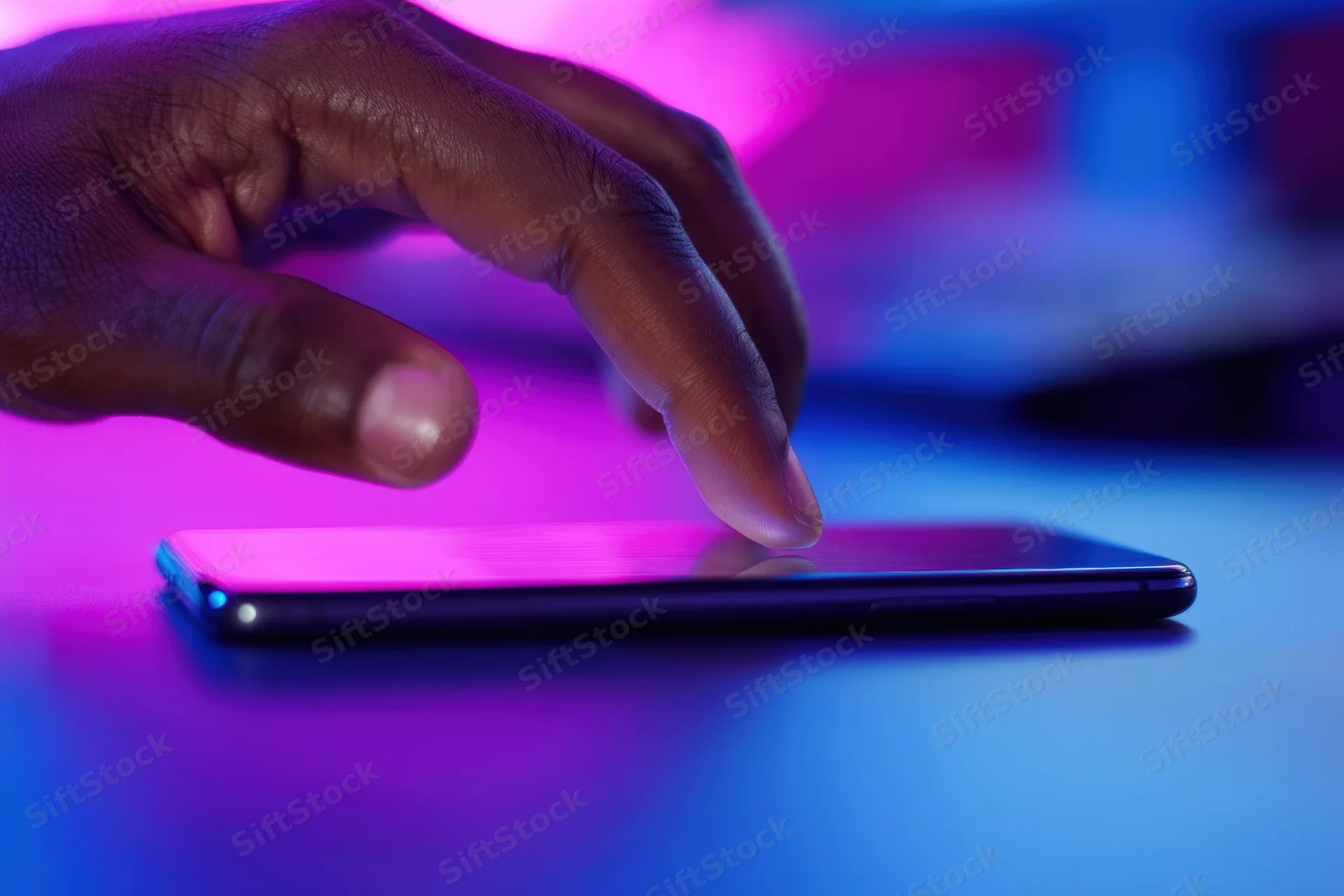 Hand tapping smartphone screen on a table under neon lighting