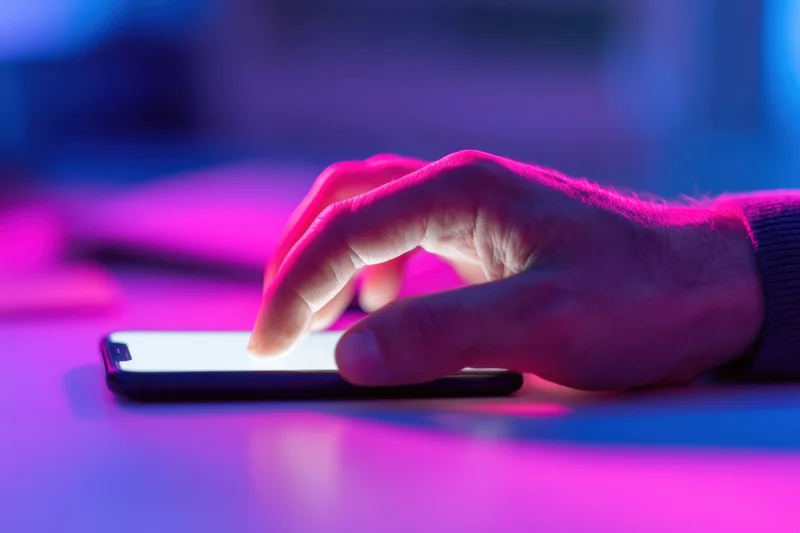 Hand tapping smartphone screen on a colorful lit surface