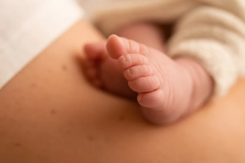 Newborn baby feet with curled toes resting on adult skin