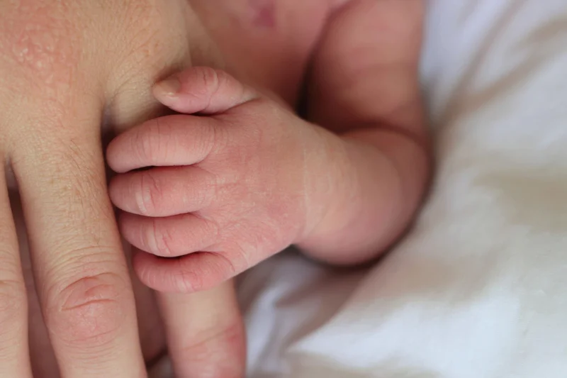 Newborn baby's tiny hand grasping an adult finger on a white blanket