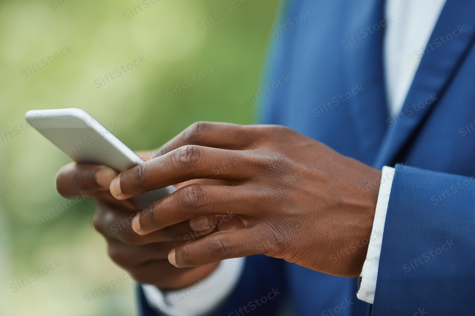 Close-up of a man's hands typing on a smartphone while wearing a blue suit outdoors
