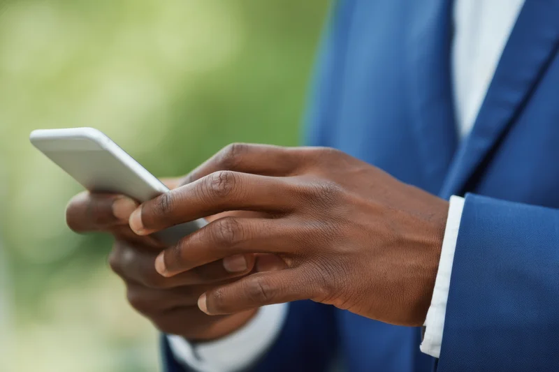 Close-up of a man's hands typing on a smartphone while wearing a blue suit outdoors