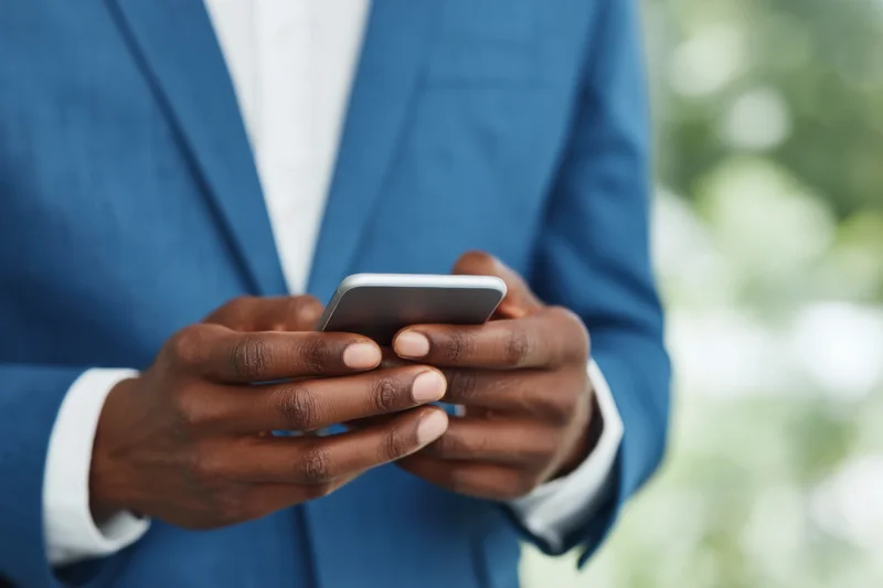 Man in blue suit typing on smartphone outdoors
