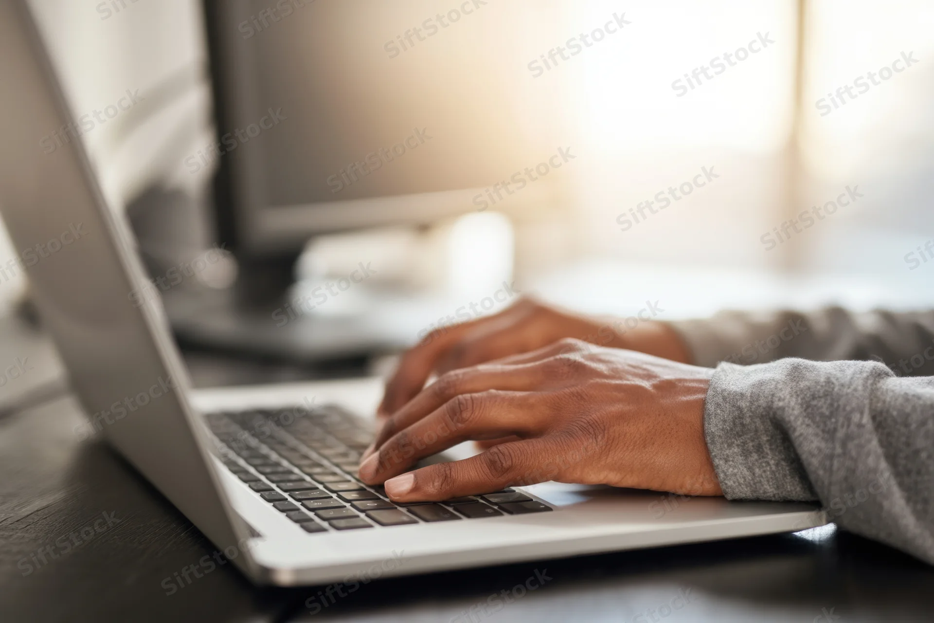 Hands typing on a laptop resting on a dark wood desk in an office setting