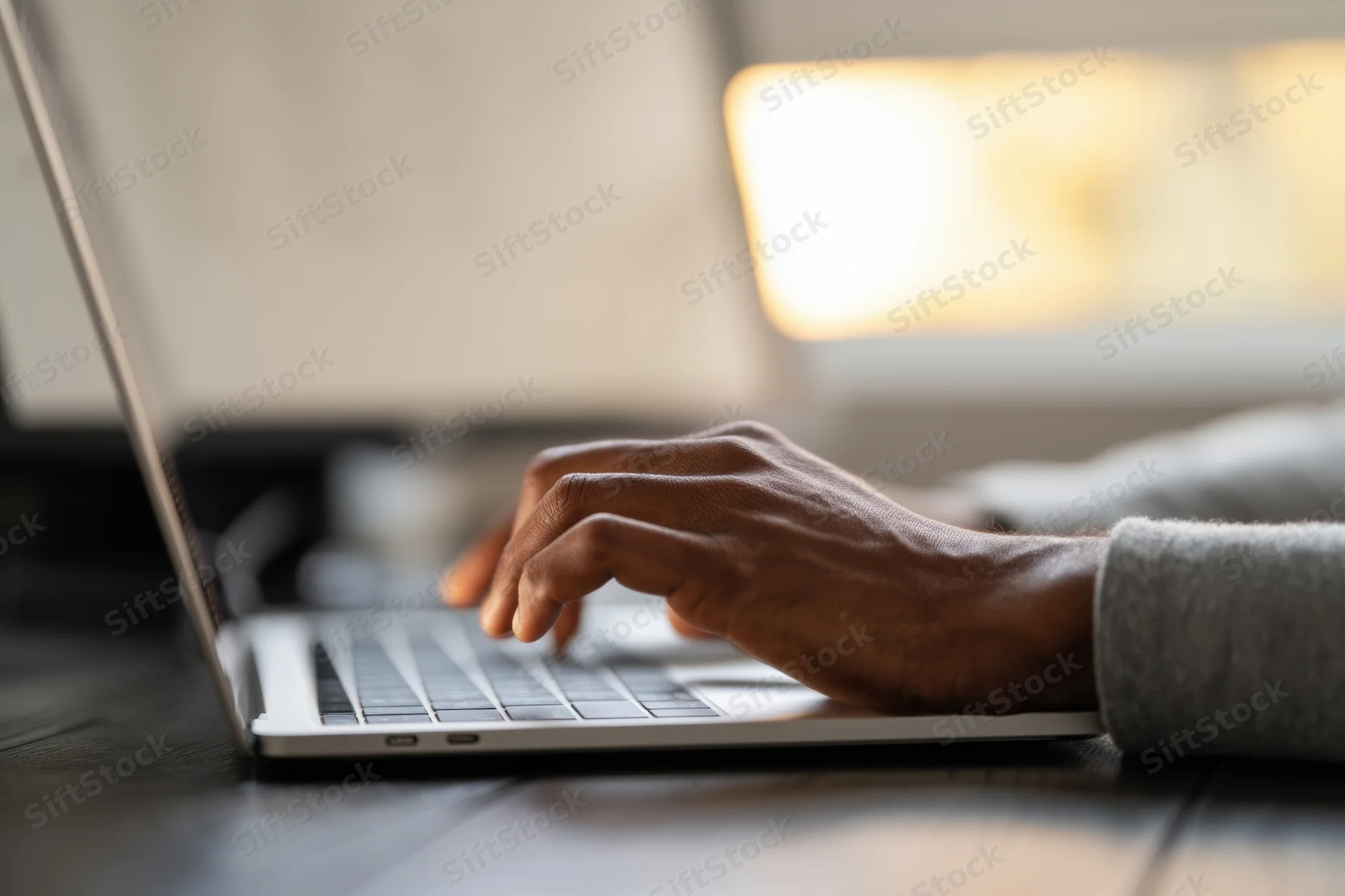 Hands typing on a laptop resting on a dark wood desk