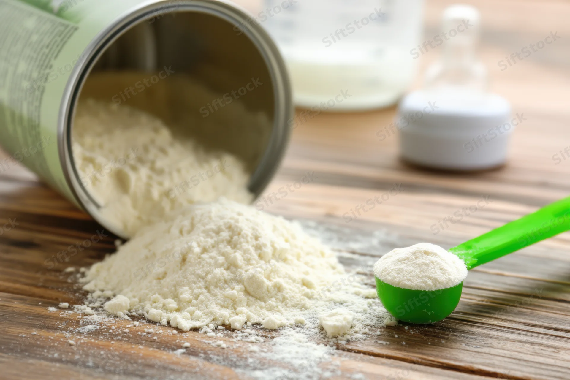 Spilled baby formula powder on wooden table with green scoop and bottle in background