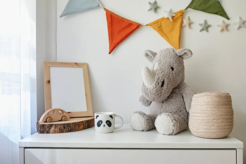 Stuffed rhinoceros toy and panda mug on white dresser with wooden car and mirror frame in nursery setting