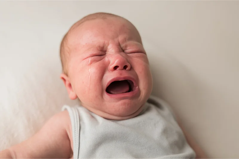 Crying newborn with eyes squeezed shut and mouth open in a wail lying on a plain surface