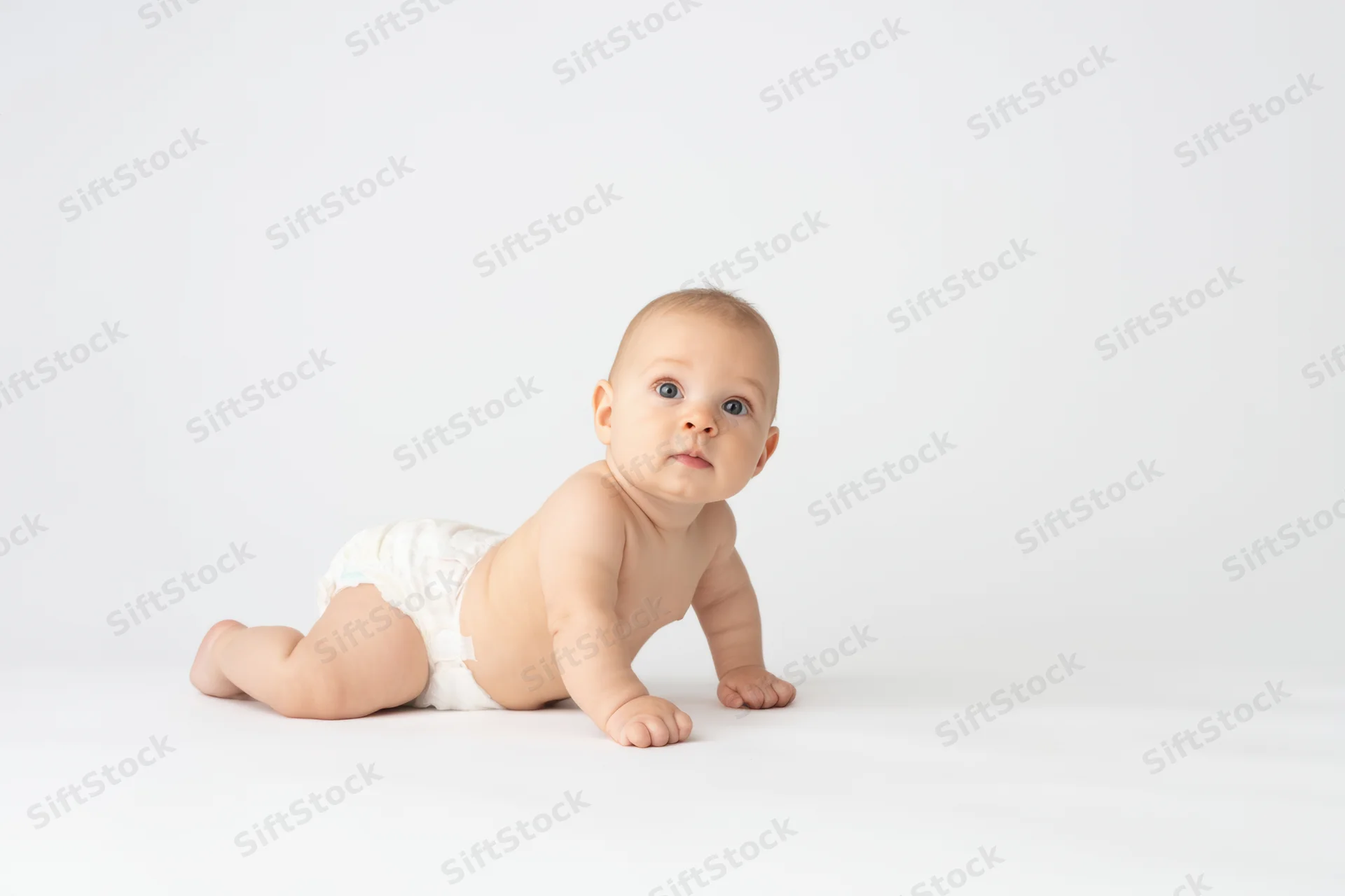 Baby crawling on white studio floor in diaper, looking up with curious expression