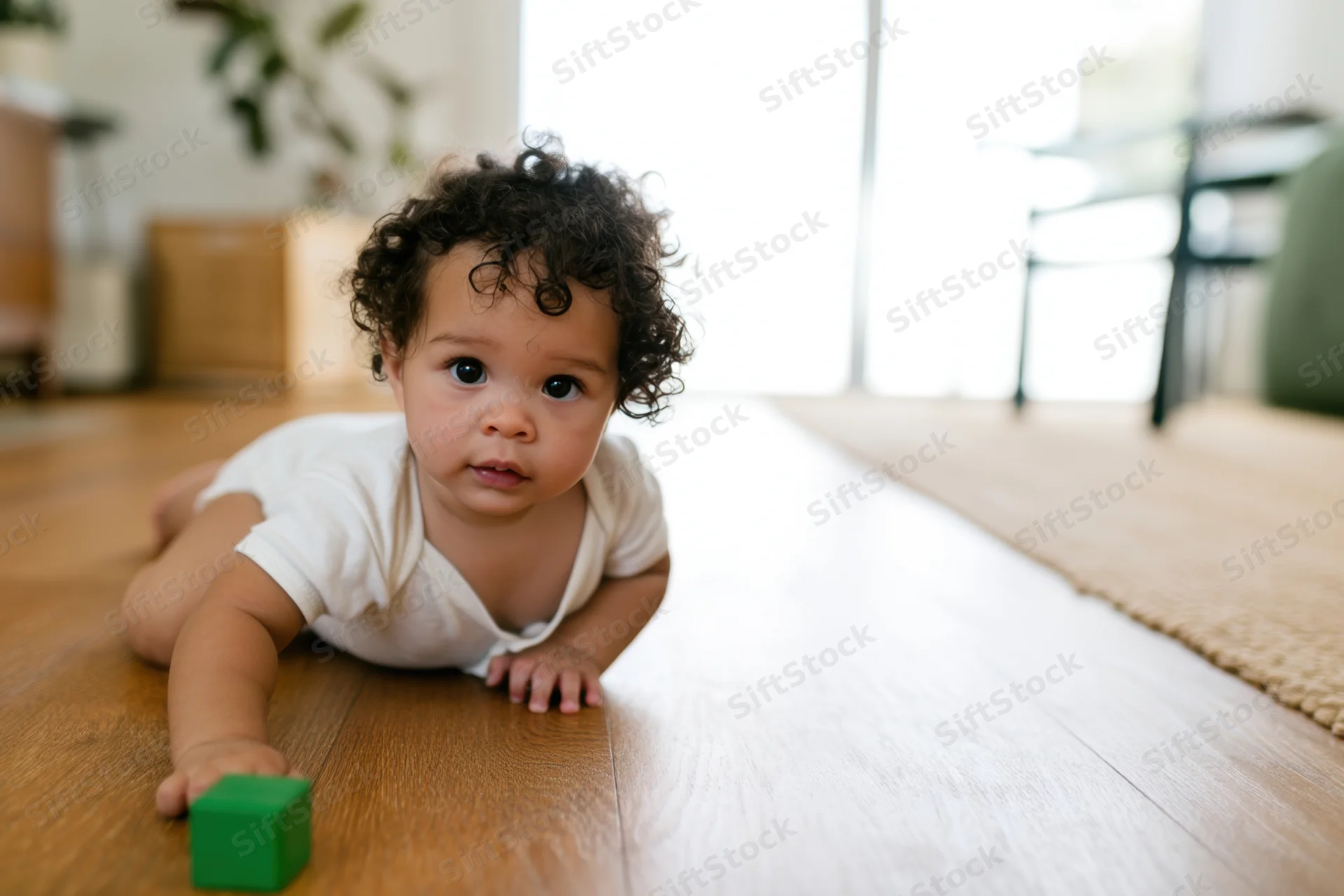 Toddler crawling on wooden floor with green block in hand
