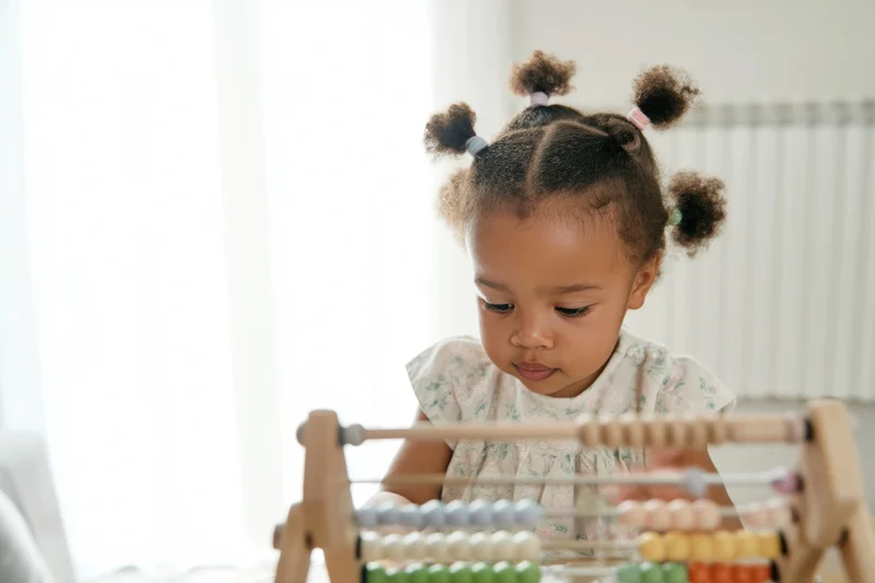 Toddler girl concentrating on counting colorful beads on wooden abacus indoors