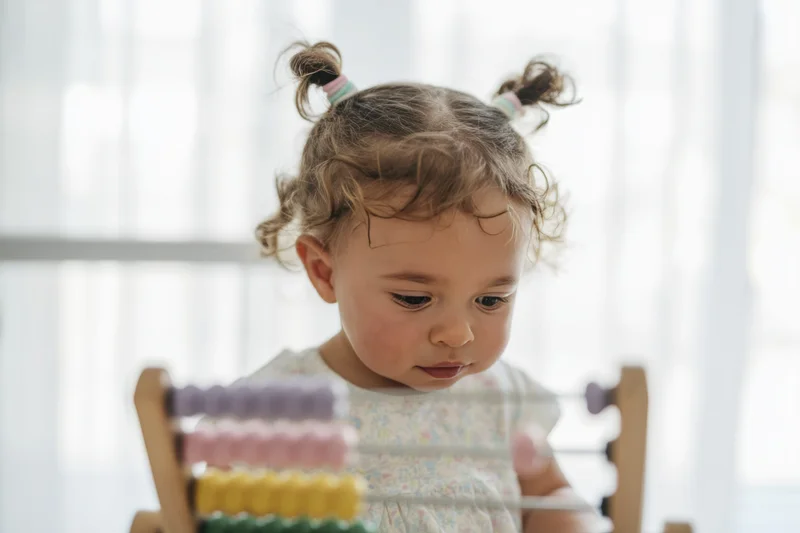 Toddler concentrating on a wooden abacus with colorful beads at a table indoors