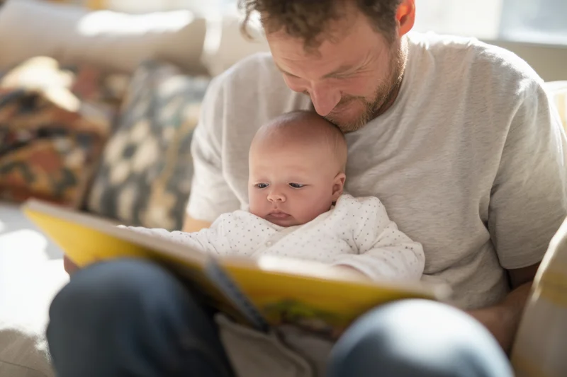 Father reading a book to baby on his lap at home
