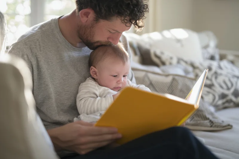 Father reading a yellow book to baby on his lap at home