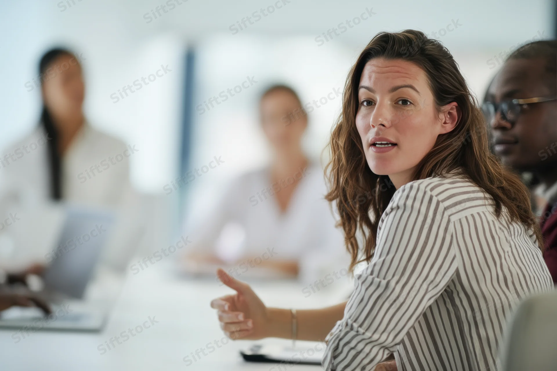 Woman speaking and gesturing during office meeting with colleagues around table