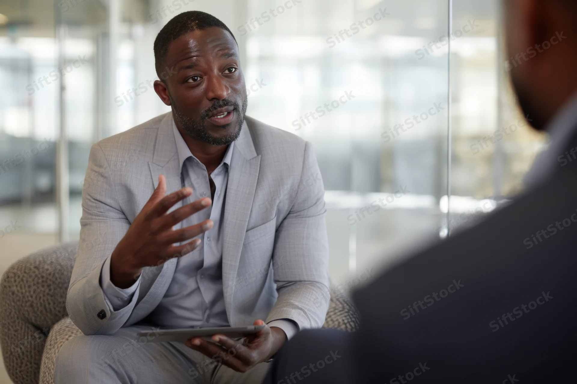 Man in gray suit gesturing with tablet during office meeting
