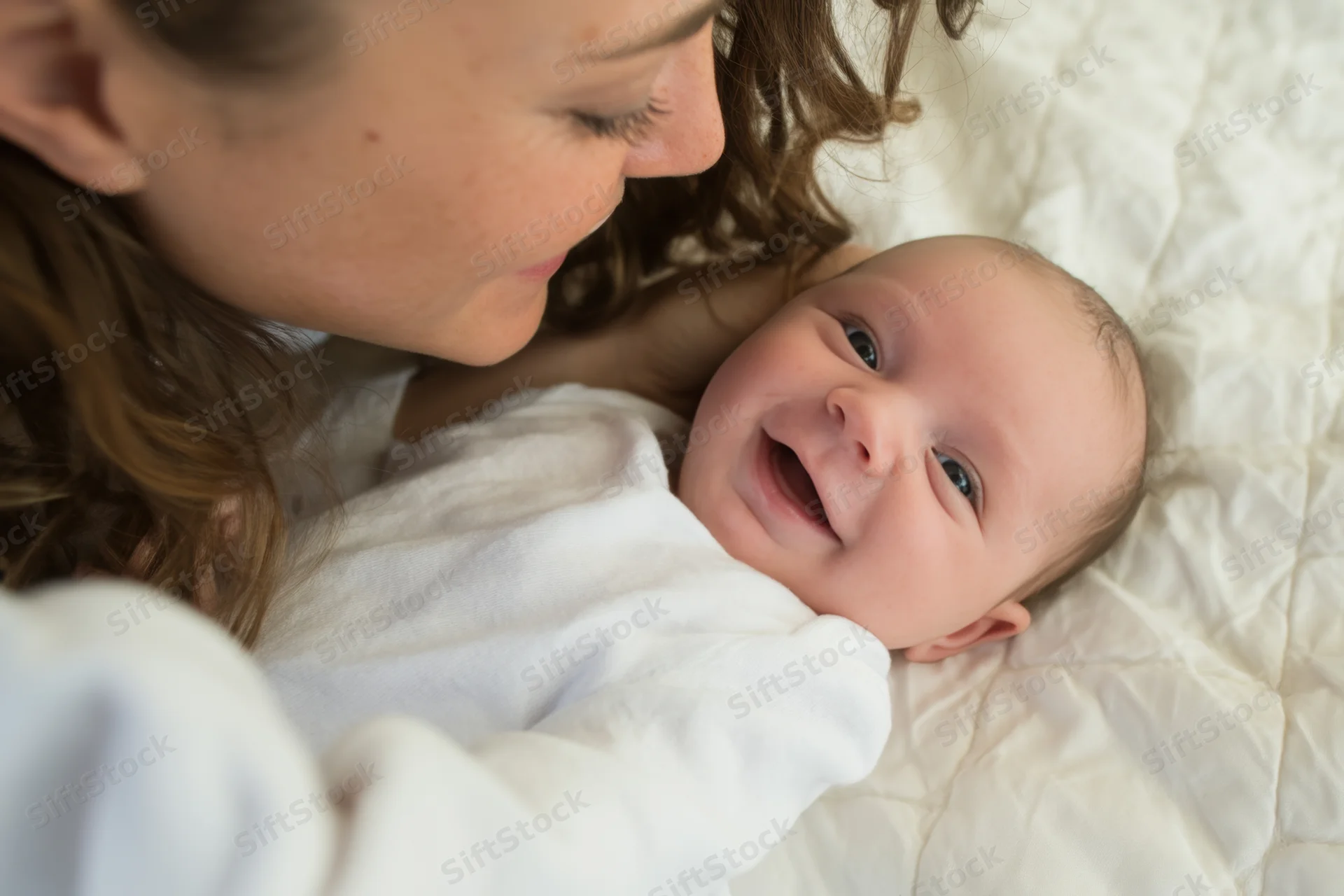 Mother cradling smiling newborn on soft quilted bedding