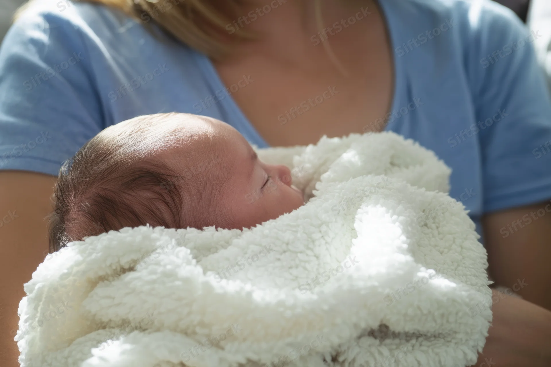 Newborn baby sleeping peacefully wrapped in a fluffy white blanket held by a woman