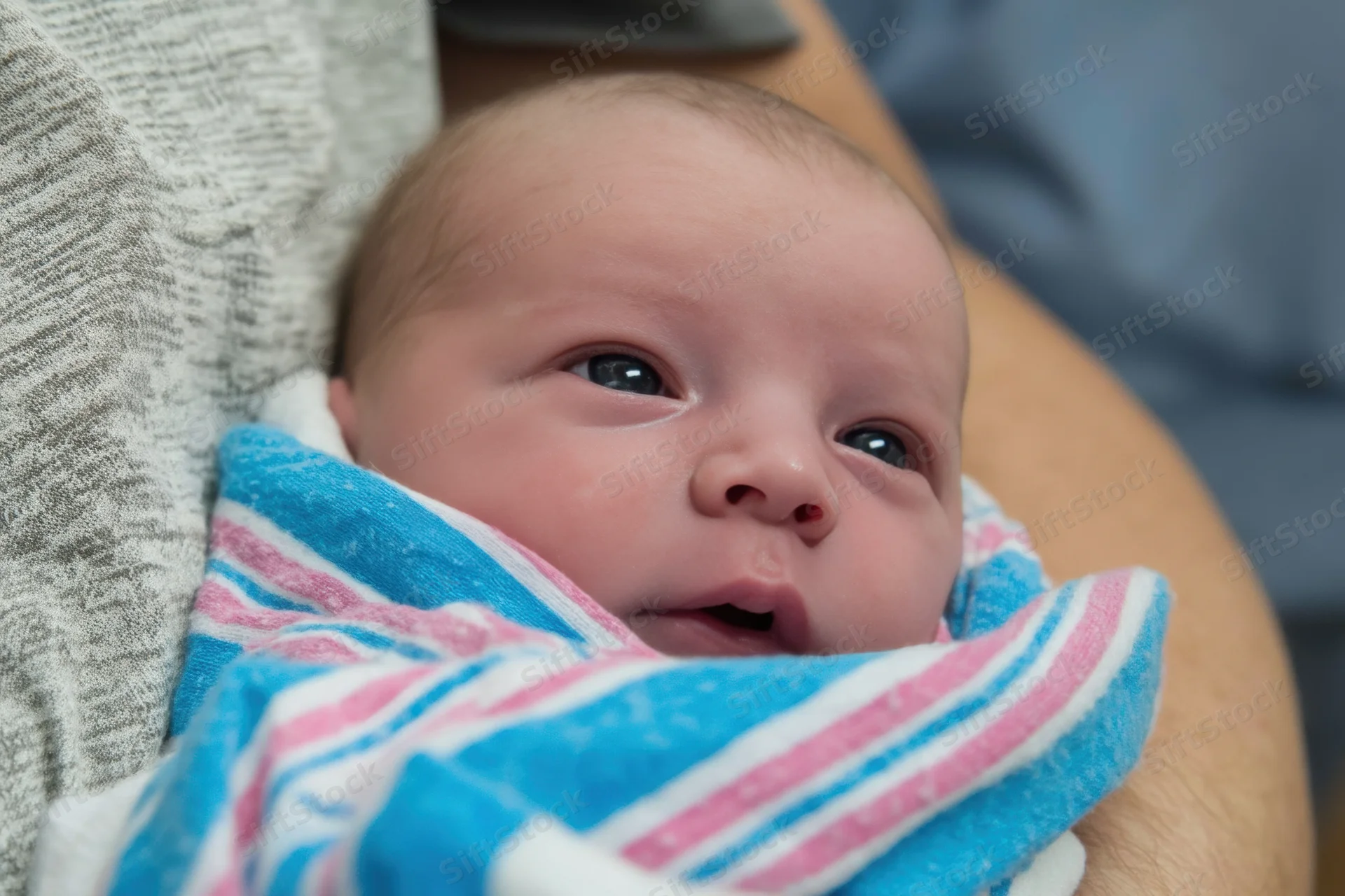 Newborn baby wrapped in blue and pink striped blanket held in adult arms