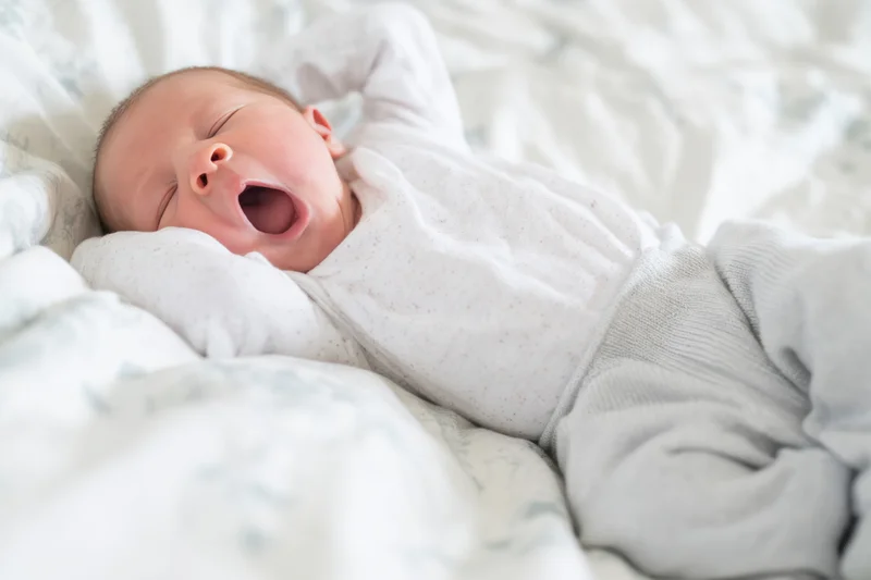 Newborn baby yawning and stretching on a soft patterned blanket